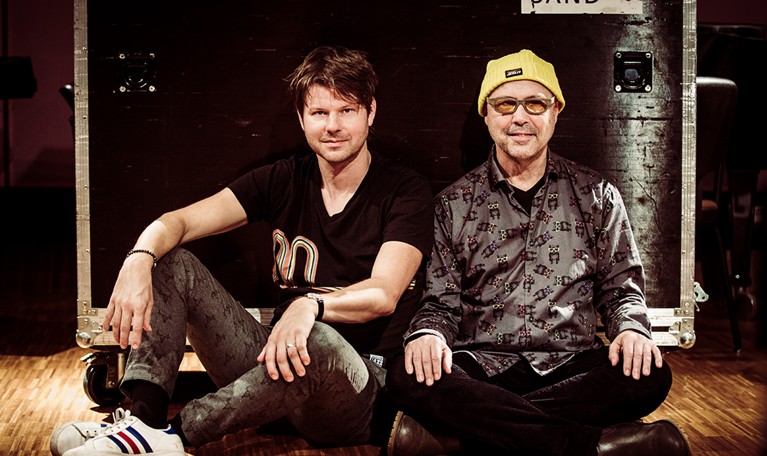 Två män som sitter på ett golv. Fotografi.